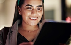 Mulher sorridente usando headphones e lendo um tablet, com foco na expressão feliz e conteúdo digital, promovendo o uso de tecnologia com Wi-Fi seja bem-vindo.