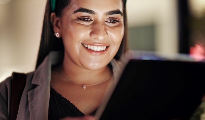Mulher sorridente usando headphones e lendo um tablet, com foco na expressão feliz e conteúdo digital, promovendo o uso de tecnologia com Wi-Fi seja bem-vindo.